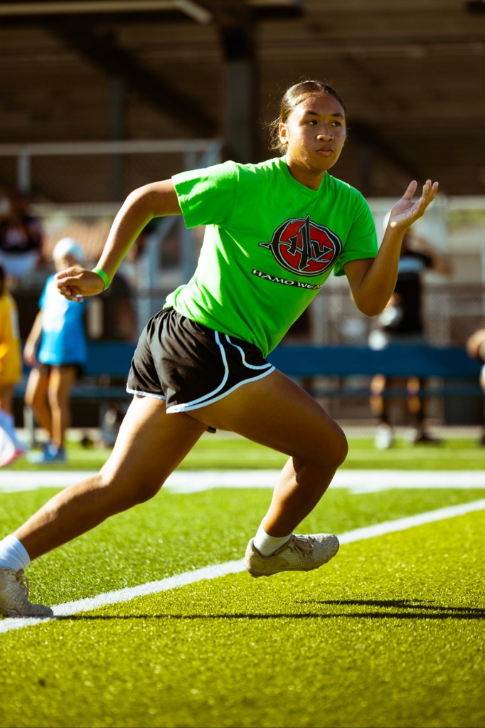 Pualani Olotoa-Le'au in her green Hamo Wear shirt sprinting on the turf