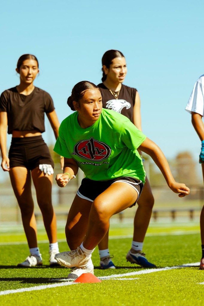 Pualani Olotoa-Le'au in her green Hamo Wear shirt in an athletic stance at a cone on the turf